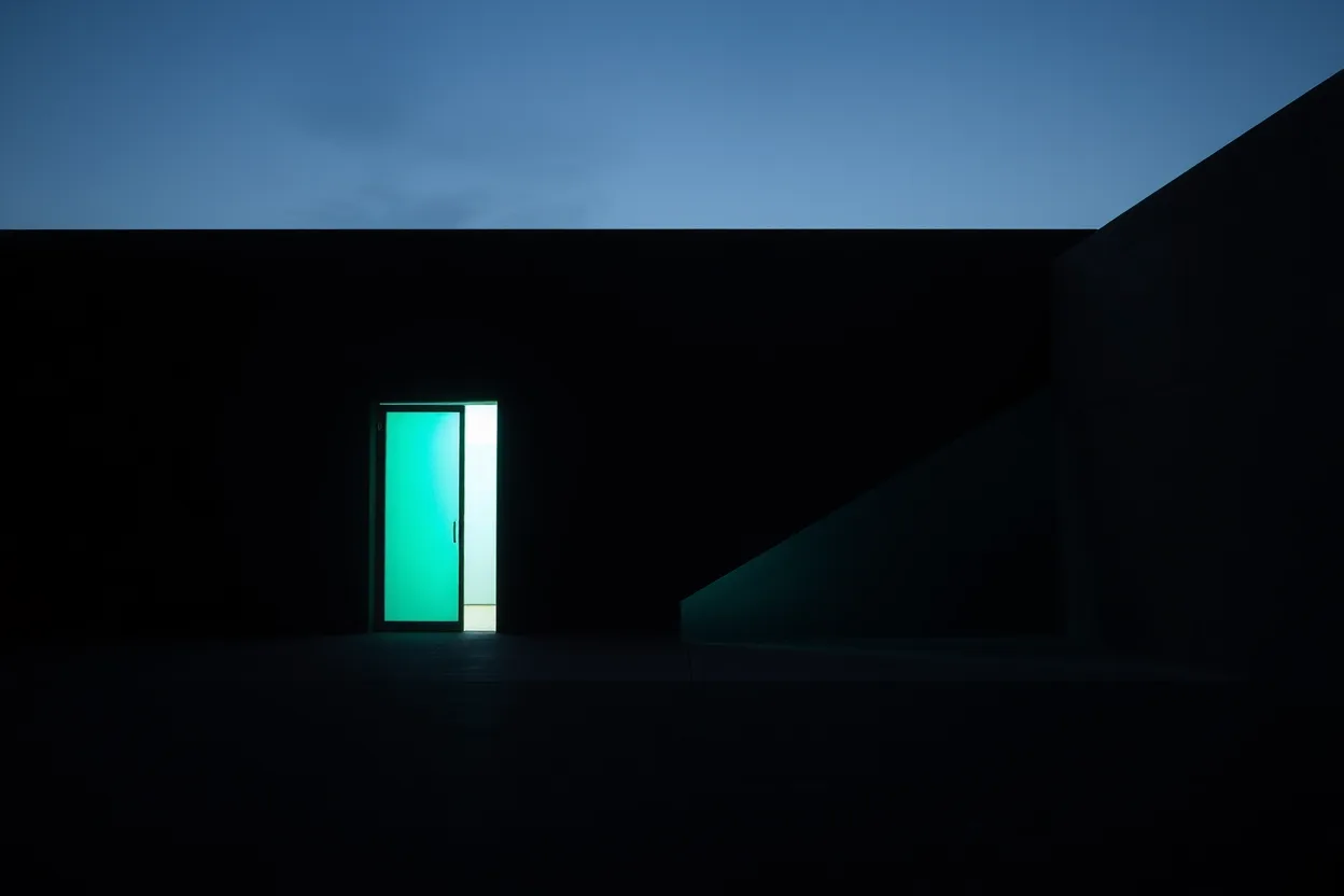 A teal-lit doorway standing in a long dark elevation beneath a pale band of dusk sky.